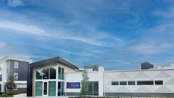 Exterior view of modern medical facility showing main entrance with glass doors, contemporary white and tan facade, and landscaping