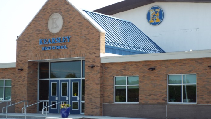 Exterior of Kearsley High School main entrance showing brick construction, blue signage, glass doors, and landscaped entry area