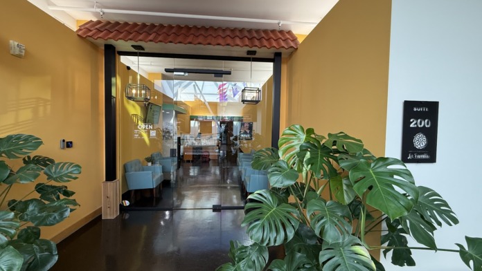 Interior foyer showing yellow walls, glass entrance doors, seating area, and lush greenery with Suite 200 branding