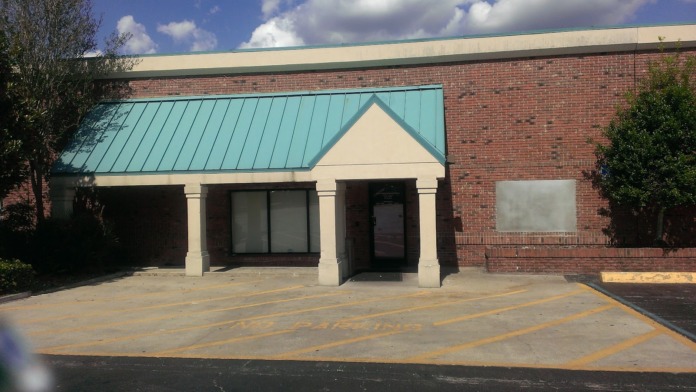 Exterior entrance of treatment center showing brick building with turquoise metal roof, cream portico, and parking area