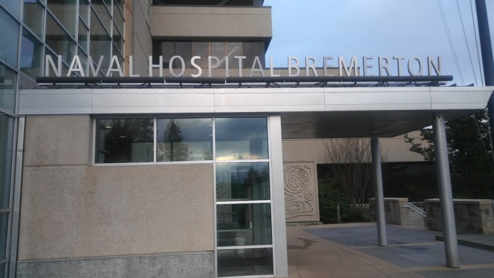 Exterior front entrance with Naval Hospital Bremerton signage, glass doors, and modern facility facade