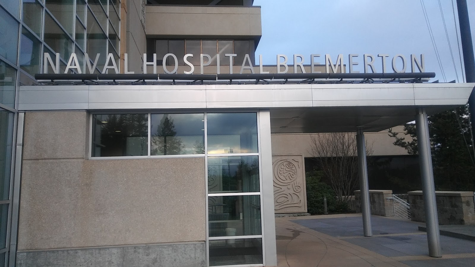 Exterior front entrance with Naval Hospital Bremerton signage, glass doors, and modern facility facade