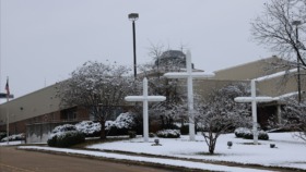 Exterior winter view of facility entrance with white crosses, landscaping, and brick building facade
