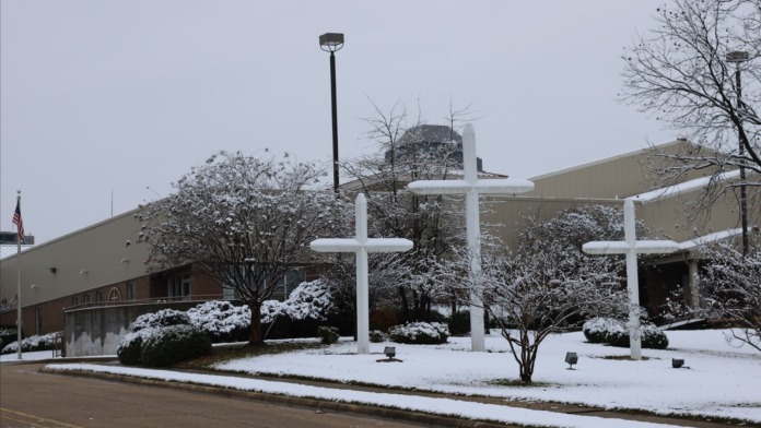 Exterior winter view of facility entrance with white crosses, landscaping, and brick building facade
