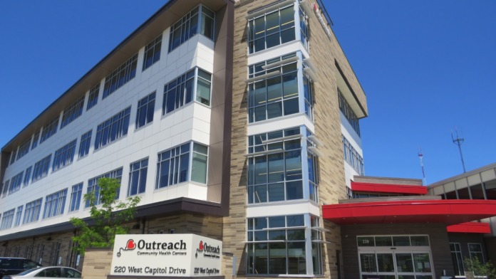 Exterior view of Outreach Community Health Centers multi-story building with stone and white facade, main entrance, and parking area