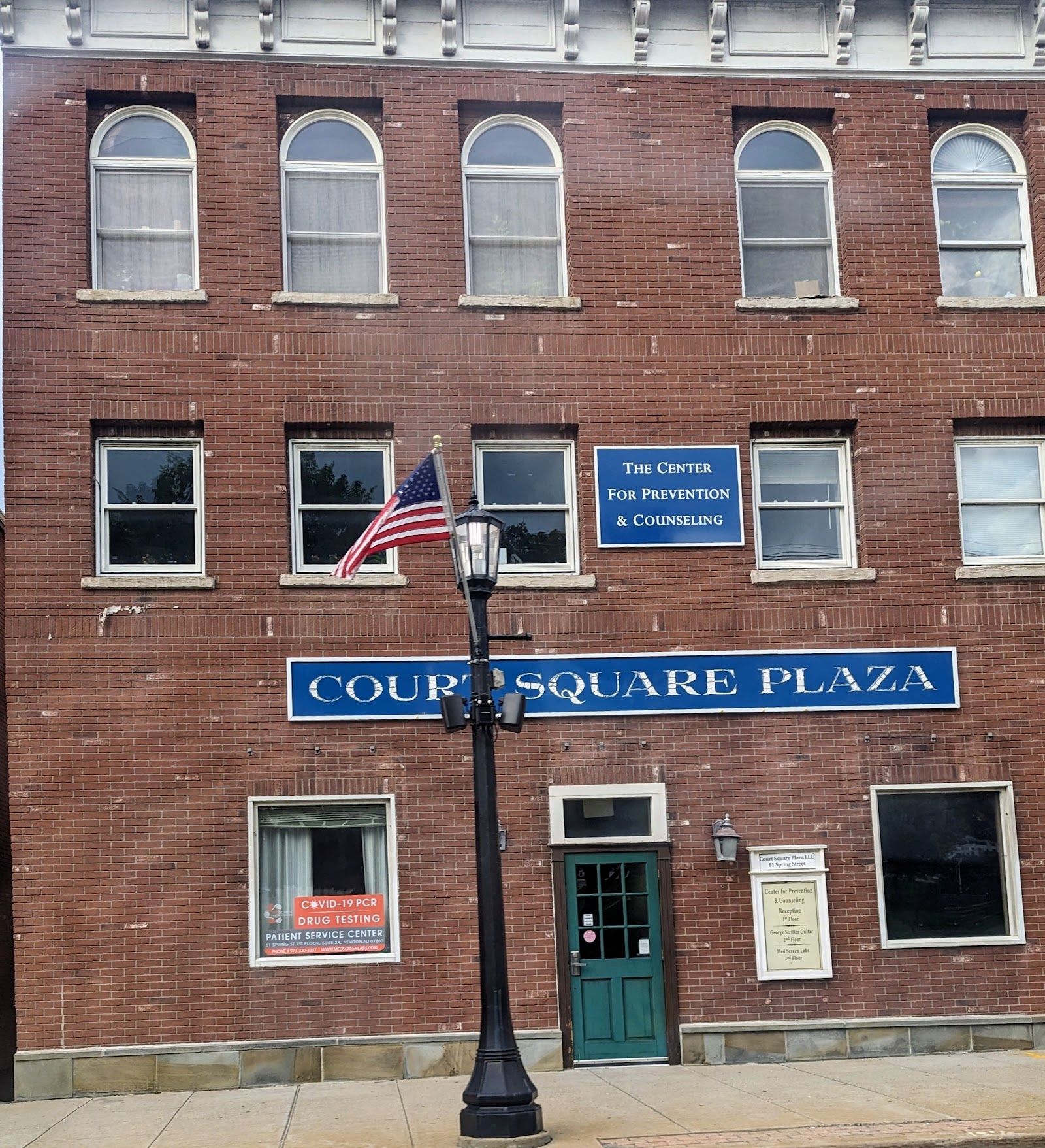 Exterior view of brick building showing main entrance with green door, facility signage, and street-level storefront