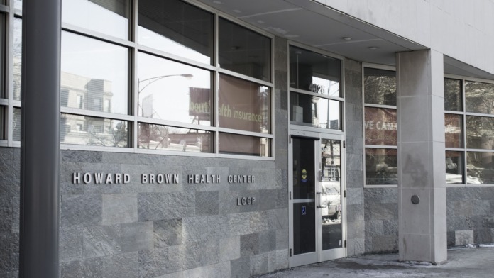 Exterior of Howard Brown Health Center showing stone facade, main entrance door, and facility name signage on building wall