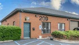 Exterior showing red brick building with entrance door, address 209, windows, and accessible parking spaces