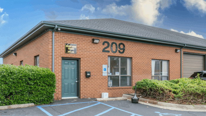 Exterior showing red brick building with entrance door, address 209, windows, and accessible parking spaces