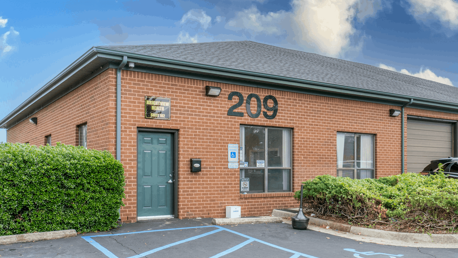 Exterior showing red brick building with entrance door, address 209, windows, and accessible parking spaces