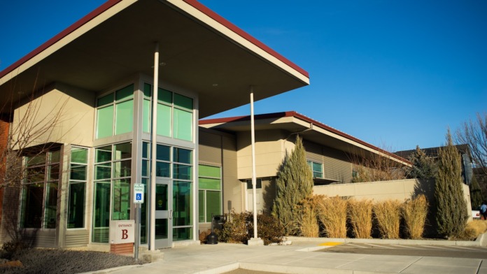 Exterior view of Terry Reilly Health Services building with main entrance, red roof, landscaping, and parking area