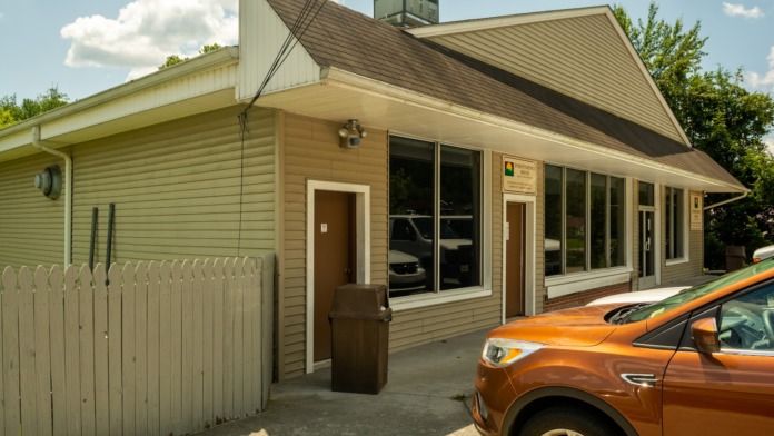 Exterior view of treatment facility showing main entrance with tan siding, large windows, parking area, and facility signage