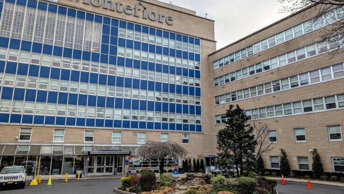 Exterior view of Montefiore Medical Center showing main brick facade with blue-windowed tower section and landscaped entry area