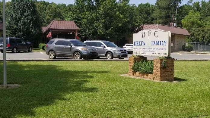 Exterior showing facility entrance with Delta Family Clinic signage, parking area with vehicles, and building facade