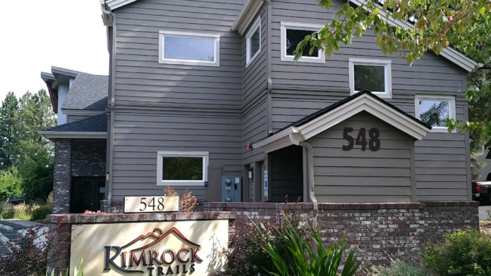 Exterior front entrance of treatment facility with gray residential building, brick base, and Rimrock Trails signage with address 548.