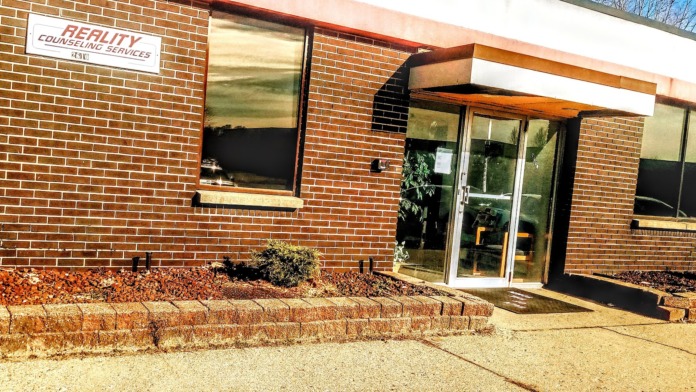 Exterior view of brick building with Reality Counseling Services sign, entrance doors, and landscaped grounds
