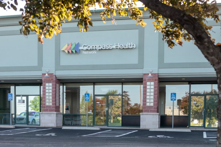 Exterior view of Compass Health Network treatment center with main entrance, glass doors, and illuminated signage