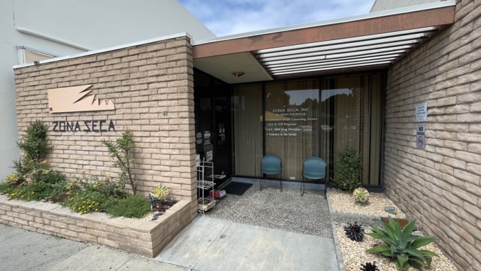 Exterior view of Zona Seca treatment center entrance with brick facade, signage, glass doors, and landscaped courtyard
