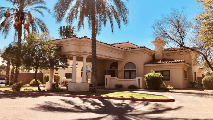 Exterior front entrance with tan stucco facade, arched windows, columns, palm trees, and landscaping
