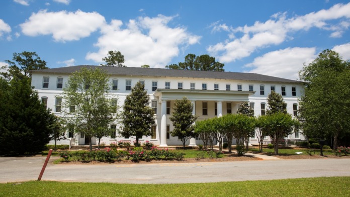 Exterior view of white colonial-style treatment facility building with covered portico, manicured landscaping, and mature trees