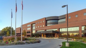 Exterior view of brick building entrance with flagpoles, landscaped grounds, and modern architectural design