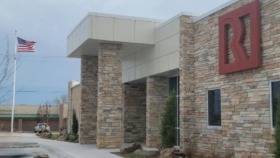 Exterior view of Native American Center of Recovery showing brick and stone front entrance with blue doors, landscaping, and American flag