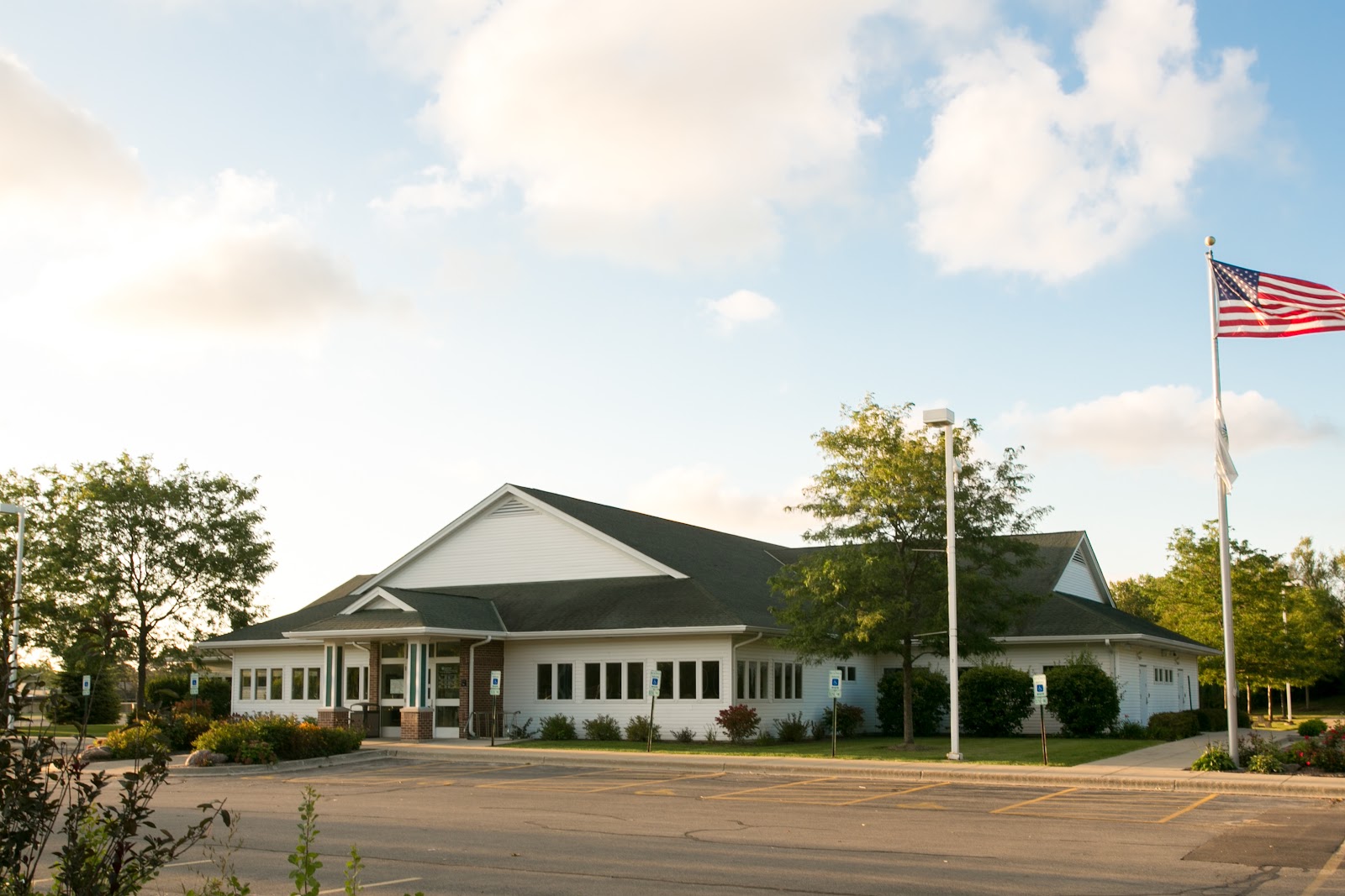 Exterior view of health center main entrance with white building, brick accents, gabled roof, landscaping, and parking area