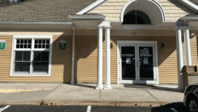Exterior front entrance of treatment facility with columned portico, double glass doors, and tan siding