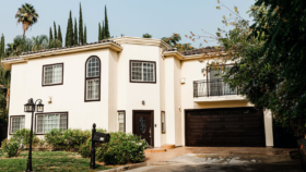 Exterior view of cream-colored residential building with dark trim, arched entry door, and manicured landscaping