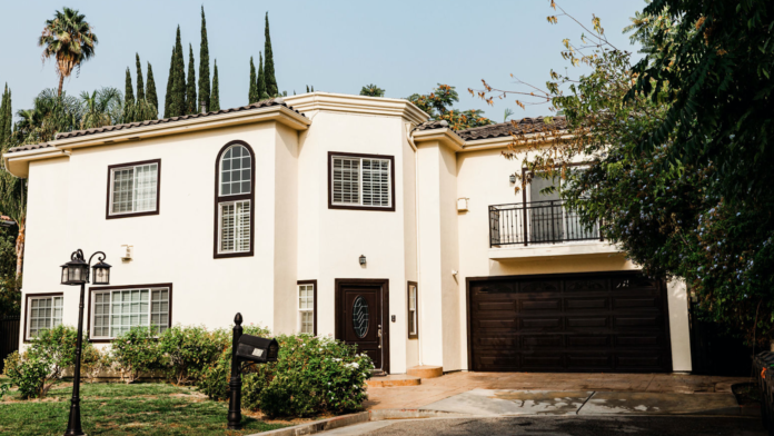 Exterior view of cream-colored residential building with dark trim, arched entry door, and manicured landscaping