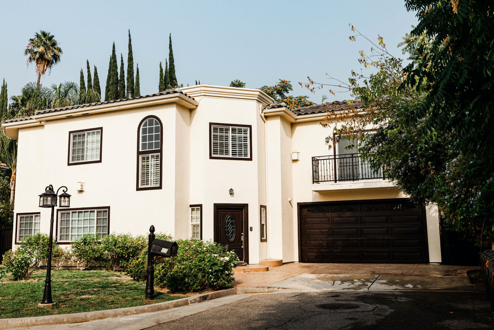 Exterior view of cream-colored residential building with dark trim, arched entry door, and manicured landscaping