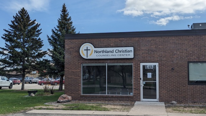 Exterior view of brick building with Northland Christian Counseling Center signage, entrance door, large windows, parking lot, and landscaping