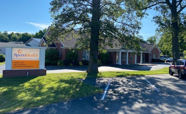 Exterior view of Spero Health Jeffersonville facility showing brick building, entrance sign, parking area, and mature trees