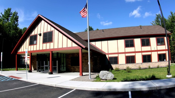 Exterior view of treatment center main entrance with red and cream timber-frame architecture, American flag, and landscaped grounds