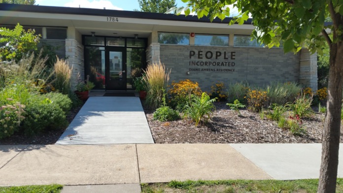 Exterior of stone building with main entrance, People Incorporated signage, landscaped front grounds, mature trees and shrubs