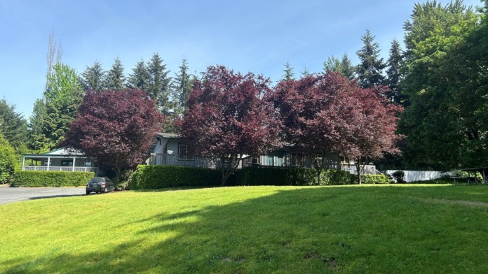 Exterior front view of residential treatment building with extended lawn, blooming ornamental trees, landscaping, and covered entry