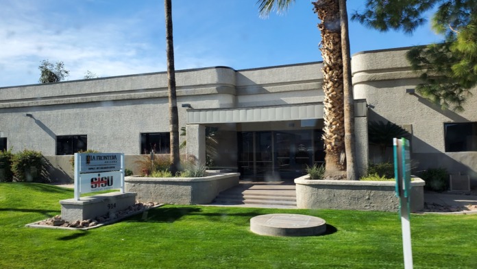 Exterior front entrance with manicured lawn, palm trees, stone signage, and facility entrance doors