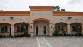 Exterior view of treatment facility with peach and orange striped facade, arched entryways, landscaping, and paved parking area