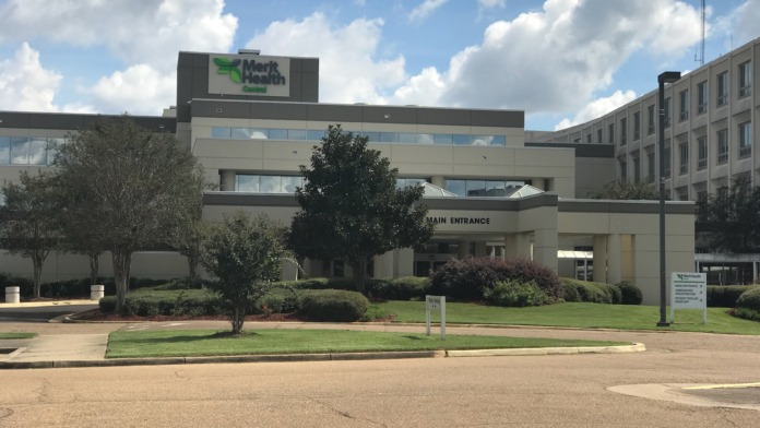 Exterior of two-story medical facility with Merit Health signage, manicured landscaping, and visitor parking area.