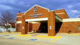 Exterior front entrance of hospital with red brick facade, HSHS Good Shepherd Hospital signage, covered drop-off area, and accessible parking spaces