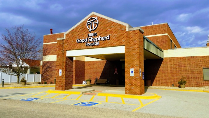 Exterior front entrance of hospital with red brick facade, HSHS Good Shepherd Hospital signage, covered drop-off area, and accessible parking spaces