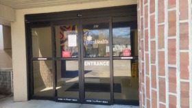Exterior main entrance showing SperoHealth signage, address number 220, glass doors with entrance marking, and brick facade
