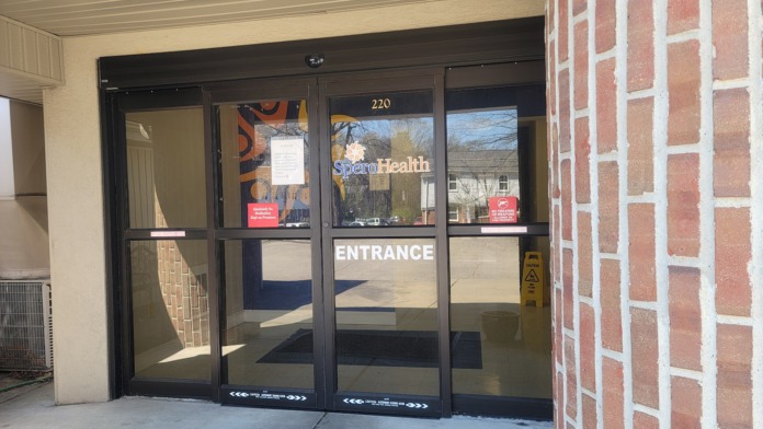 Exterior main entrance showing SperoHealth signage, address number 220, glass doors with entrance marking, and brick facade
