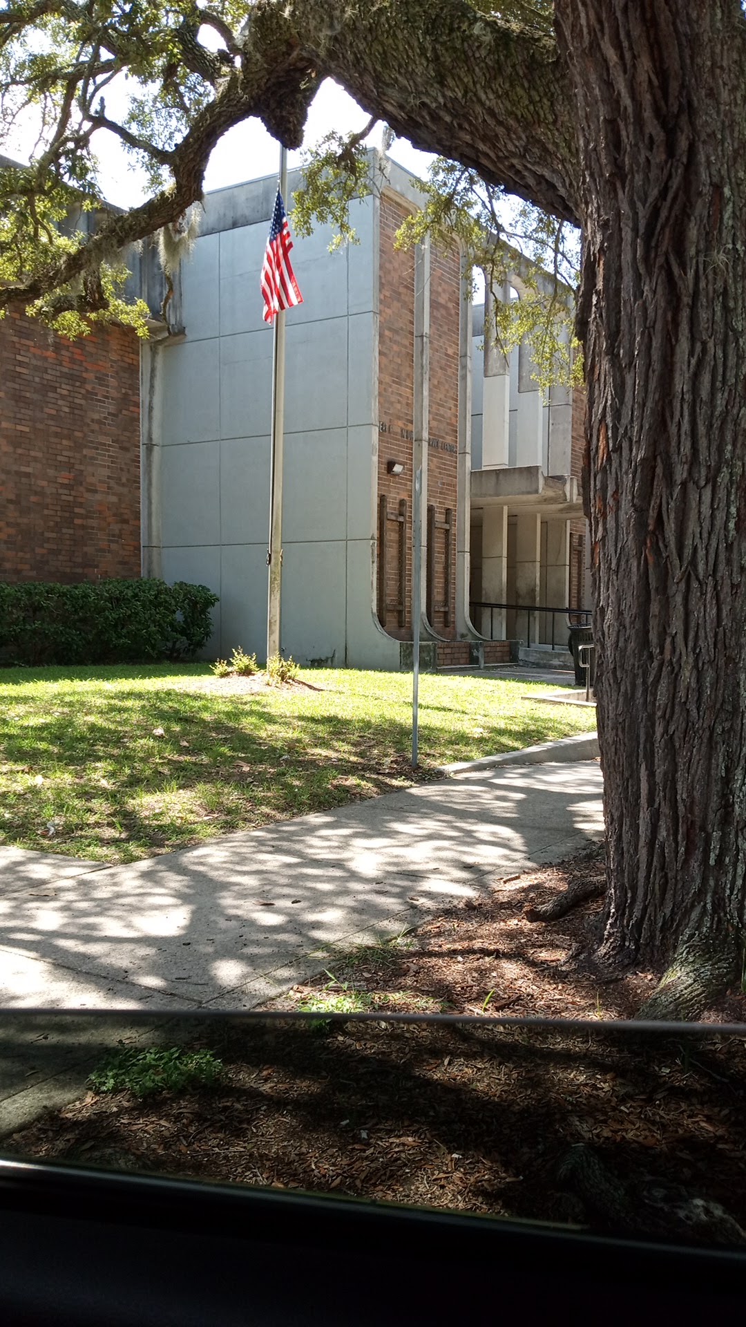 Exterior entrance featuring brick building, mature oak tree with Spanish moss, American flag, and modern metal cladding