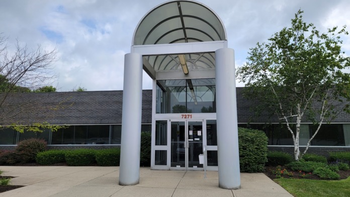 Exterior front entrance featuring modern white canopy structure with address number 7271, dark brick building facade, and landscaped grounds