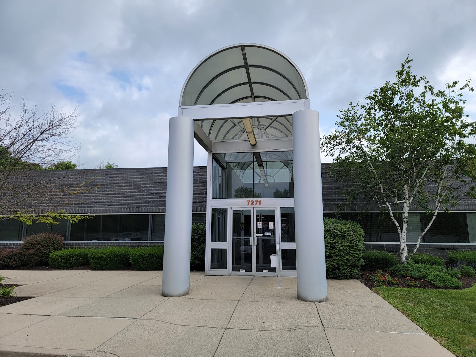 Exterior front entrance featuring modern white canopy structure with address number 7271, dark brick building facade, and landscaped grounds