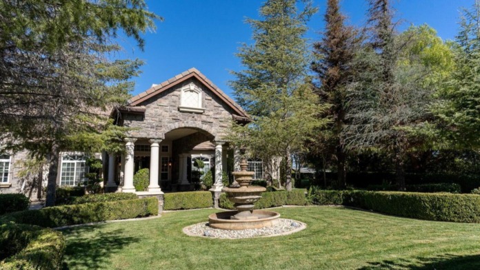 Exterior front entrance featuring stone building with white columns, arched entry, landscaped grounds with water fountain, and manicured hedges