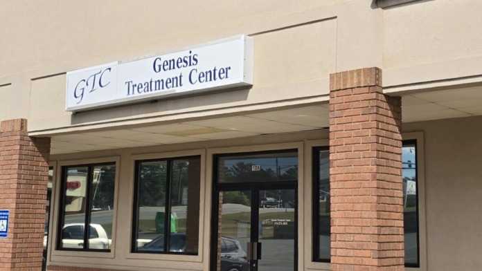 Exterior view of Genesis Treatment Center entrance with brick facade, green metal roof, glass doors, and front parking area