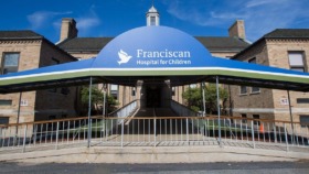 Exterior view of Franciscan Hospital for Children main entrance with blue and green canopy, brick building, and landscaping