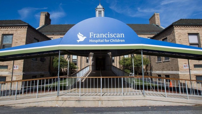 Exterior view of Franciscan Hospital for Children main entrance with blue and green canopy, brick building, and landscaping